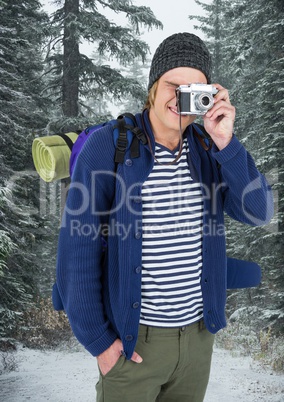 Millennial backpacker with camera against snowy trees