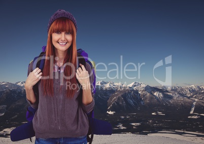 Millennial backpacker smiling against snowy mountain range