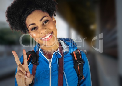 Millennial backpacker making peace sign against blurry train station