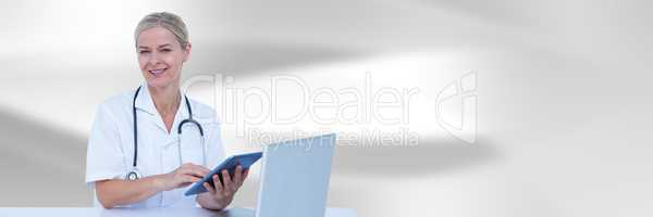 Doctor at computer with tablet against white blurred abstract background