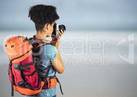Millennial backpacker with camera against blurry beach