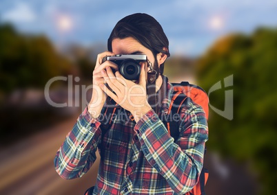 Millennial backpacker with camera against blurry road