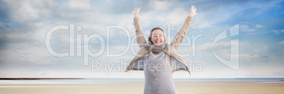 Woman in coat and scarf celebrating on beach with plane in sky