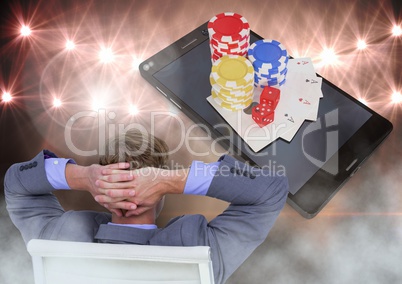 Man seated relaxed looking at phone with 3d poker chips and playing cards