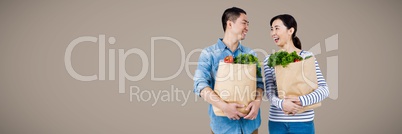 Couple laughing with grocery bags against brown background