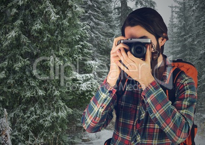 Millennial backpacker with camera against snowy trees
