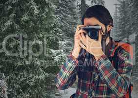Millennial backpacker with camera against snowy trees