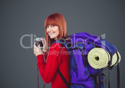 Millennial backpacker with camera against grey background