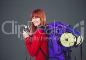 Millennial backpacker with camera against grey background