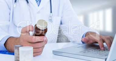 Close up of doctor holding pills at laptop against blurry window