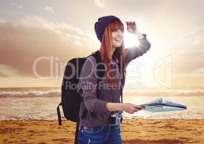 Millennial backpacker with map on sunset beach with flare