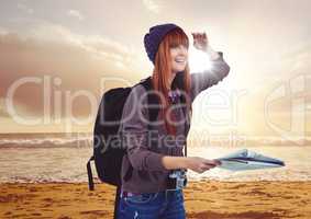 Millennial backpacker with map on sunset beach with flare
