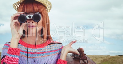 Woman looking through binoculars against landscape background