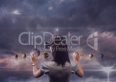 Woman in VR headset touching 3D planets against purple sky with clouds and flares