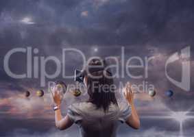 Woman in VR headset touching 3D planets against purple sky with clouds and flares