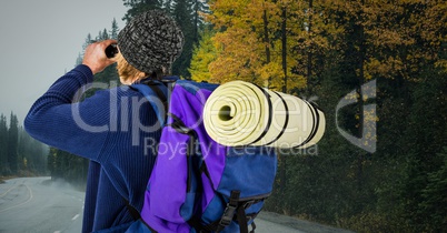 Millennial backpacker with binoculars against road with grey sky