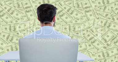 Back of business man at desk looking at green money backdrop