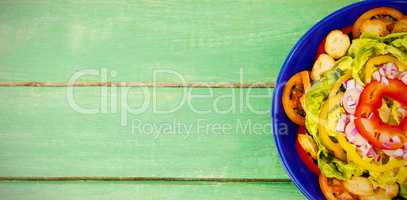 Fresh salad in blue bowl on green wooden table
