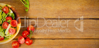 Fresh salad in bowl by tomatoes on wooden table