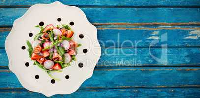 Fresh salad in white plate on blue table