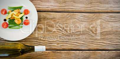 Salad in plate by wine bottle on wooden table