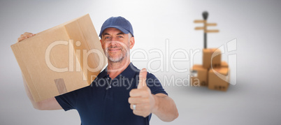 Composite image of happy delivery man holding cardboard box showing thumbs up