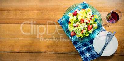 Fresh salad in bowl with red wine on wooden table