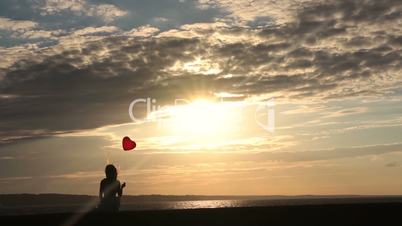 Lonely woman with heart balloon watching sunset