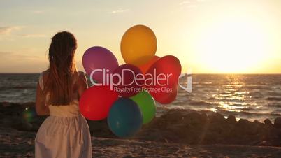 Girl with colorful balloons on beach at sunset