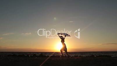 Woman running with flying scarf on beach at sunset