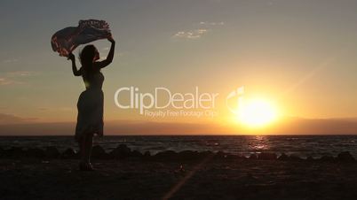 Joyful woman with flying scarf on beach at sunset