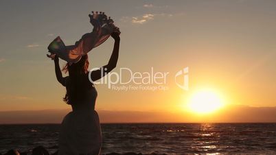 Silhouette of woman with scarf on beach at sunset