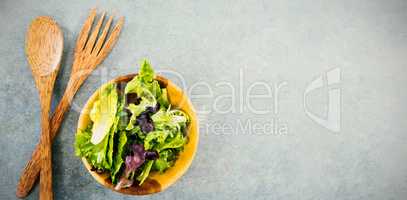 Fresh salad in bowl by wooden spoon and fork on table