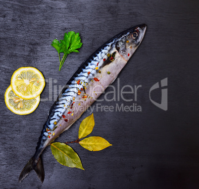 Whole fresh mackerel with spices and lemon on a black background