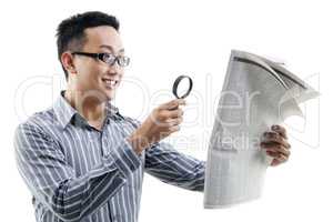 Asian man reading newspaper with magnifier