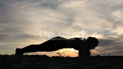 Woman doing plank hip twists on beach at sunset