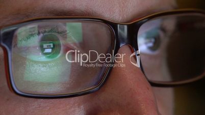 Closeup man's eyes in glasses works on laptop at night