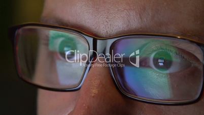 Closeup man's eyes in glasses works on laptop at night