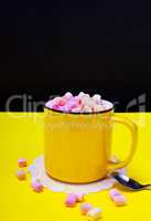 Cocoa with marshmallow in a yellow mug, next to an iron spoon