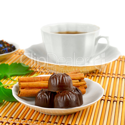 Tea cup, chocolates and cinnamon on bamboo mat on white