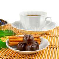 Tea cup, chocolates and cinnamon on bamboo mat on white
