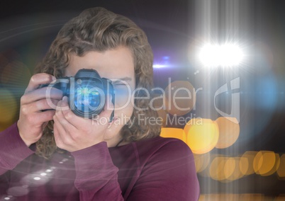 photographer man with long hair taking a photo (foreground). Blurred lights and flares behind and ov