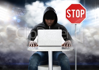 Hacker working on laptop in front of stop board