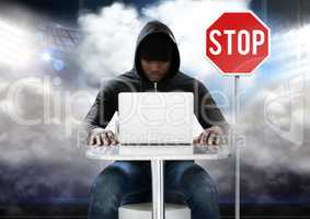 Hacker working on laptop in front of stop board
