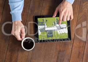 tablet with hands and coffee on a desk. On the tablet, green and grey blueprint