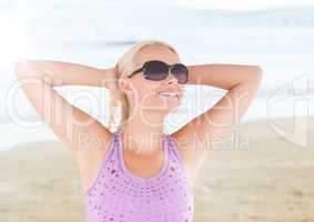 Woman in sunglasses stretching against blurry beach with flare