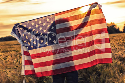 Silhouette of Young Woman Holding USA Flag in Field at Sunset