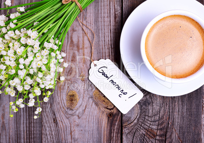 Cup of cappuccino and a bouquet of white lilies of the valley