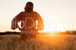 African woman in traditional clothes walking in a field of crops