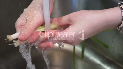 Slow motion of woman washing green onion in kitchen sink under tap water